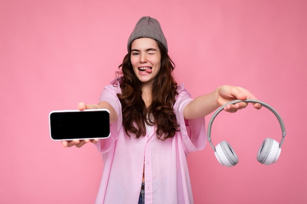 Foto de sexy muito positiva jovem morena encaracolada vestindo camisa rosa e chapéu cinza isolada