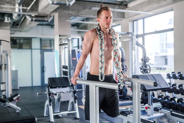 Foto de Sportsman com uma enorme corrente de metal em volta do pescoço. Flexões nas barras irregulares do ginásio