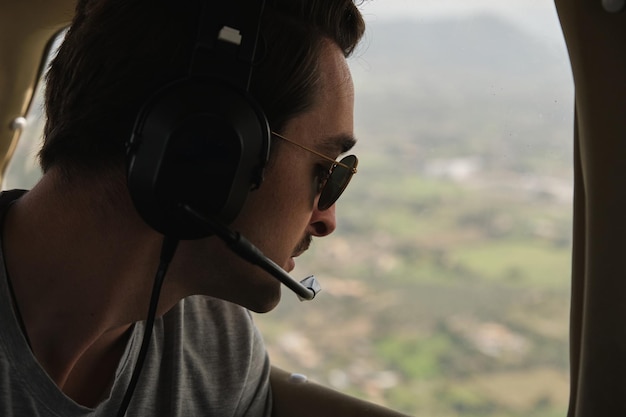 Foto de stock de homem feliz usando fone de ouvido de aviação desfrutando de um passeio de aeronave leve e olhando pela janela.