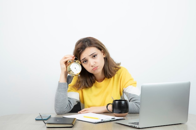 Foto de trabalhadora de escritório feminina sentada na mesa e segurando o despertador. foto de alta qualidade