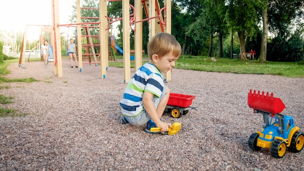 Foto de um adorável menino de 3 anos brincando com areia e seu caminhão e trailer no parque