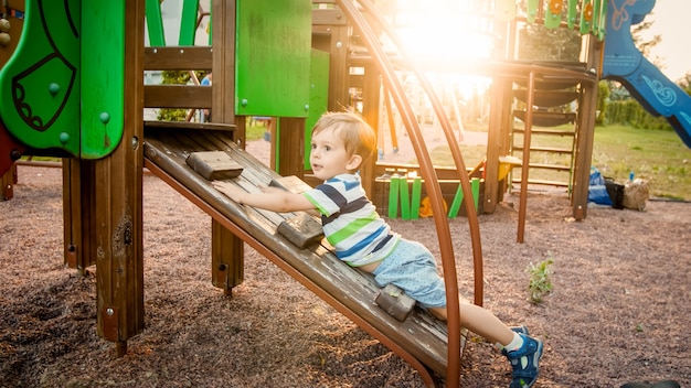 Foto de um adorável menino subindo e rastejando em uma escada de madeira no palyground infantil no parque