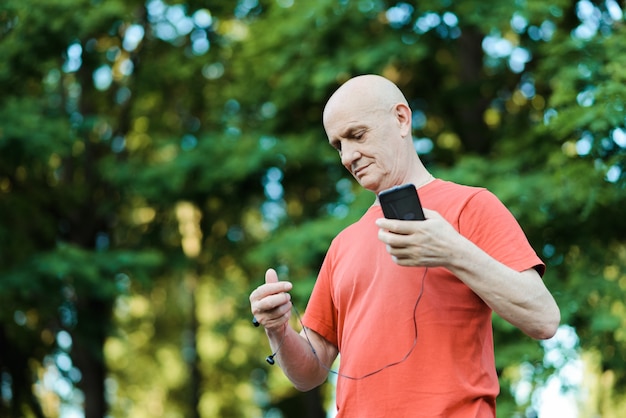 Foto de um aposentado aposentado usando fones de ouvido enquanto ouve música e tenta ouvir no parque. foto alta