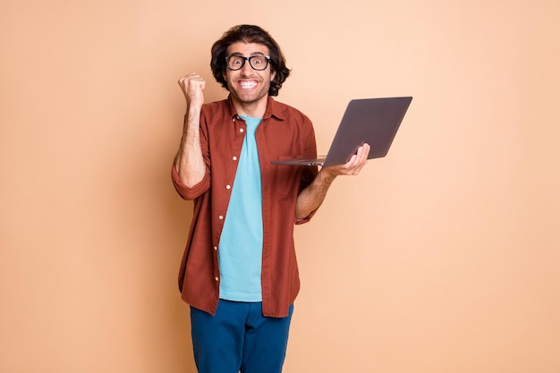 Foto de um cara animado segurando um laptop isolado em um fundo de cor bege pastel