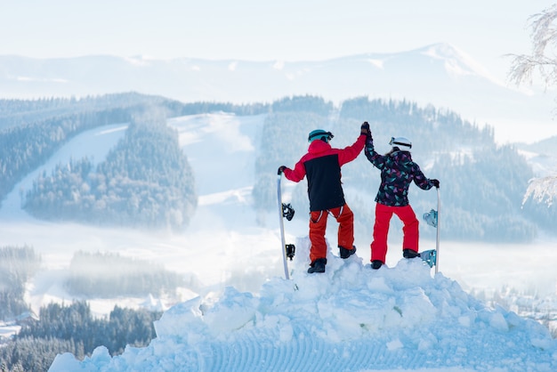 Foto de um casal alto fiving posando no topo de uma montanha de neve