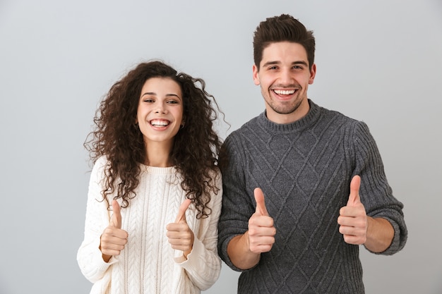 Foto de um casal feliz, homem e mulher, rindo e mostrando os polegares, isolada sobre uma parede cinza