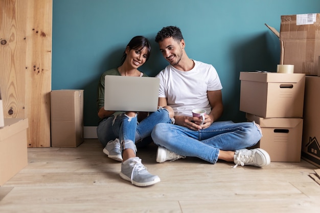 Foto de um casal jovem e atraente procurando idéias de decoração com o laptop, enquanto fazia uma pausa sentado no chão em casa.