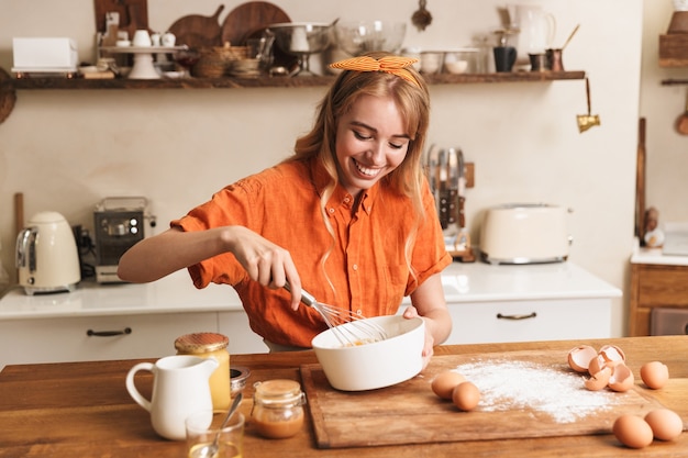 Foto de um chef feliz alegre sorridente jovem loira cozinhando na cozinha.