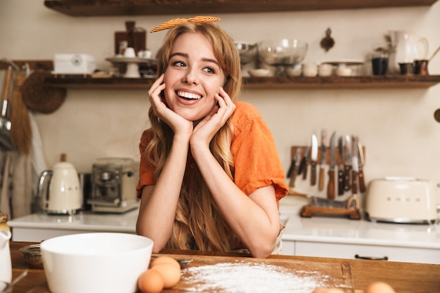 Foto de um chef feliz alegre sorridente jovem loira cozinhando na cozinha.