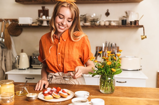 Foto de um chef sorridente alegre jovem loira cozinhando na cozinha pastelaria doce de morango.