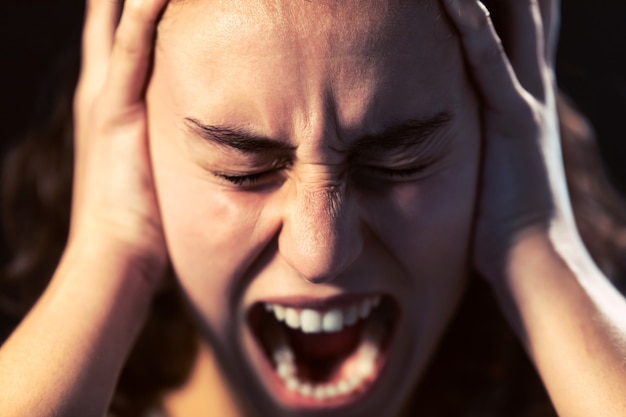 Foto de um close-up de mulher jovem gritando sobre fundo preto. Conceito de doença mental.