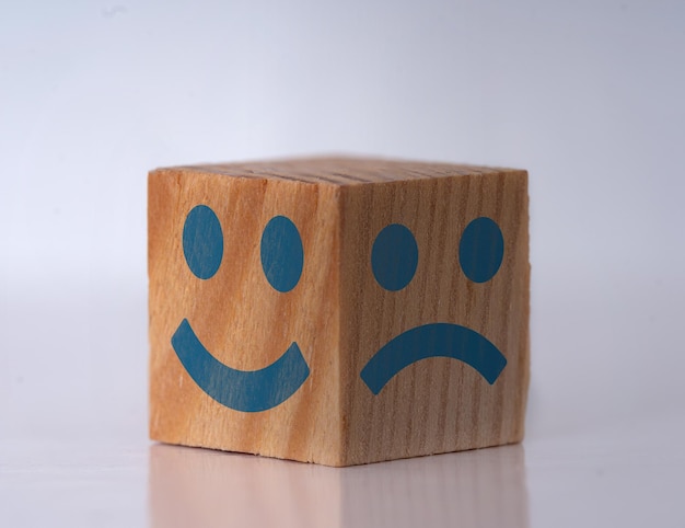 Foto de um cubo de madeira com expressões faciais felizes e tristes como símbolo de mudanças instantâneas de personalidade