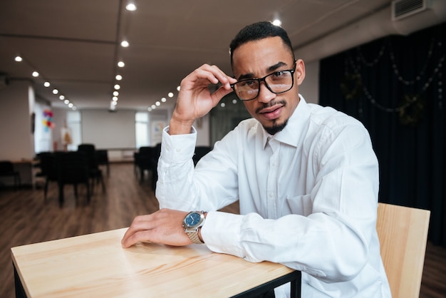 Foto foto de um empresário atraente usando óculos, sentado à mesa e olhando para a frente