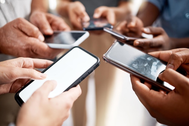 Foto de um grupo de empresários irreconhecíveis usando seus smartphones em um escritório moderno