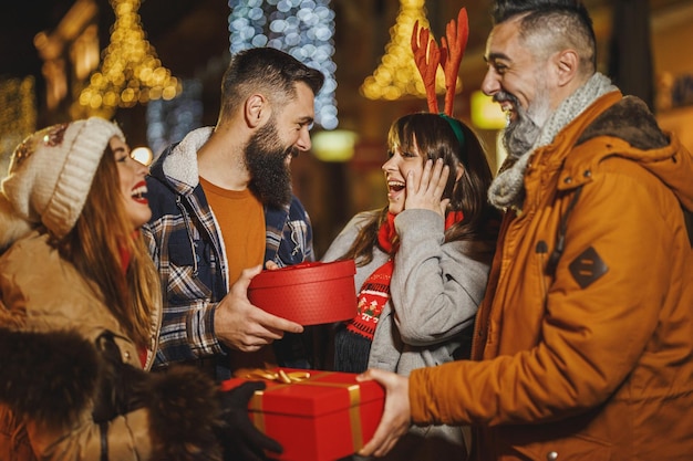 Foto de um grupo de jovens amigos alegres com presentes de Natal se divertindo em uma noite.