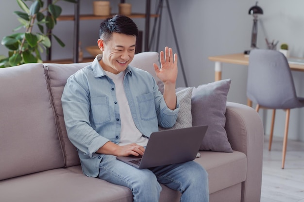 Foto de um homem amigável e sociável sentado no sofá segurar netbook onda mão câmera web usar camisa casual em casa dentro de casa