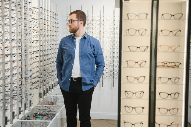 Foto de um homem barbudo bonito experimentando óculos novos na loja de óculos Homem comprando óculos Visão de saúde visão compras de moda