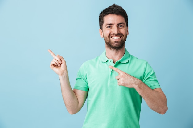 Foto de um homem barbudo bonito jovem feliz posando isolado sobre a parede azul apontando.