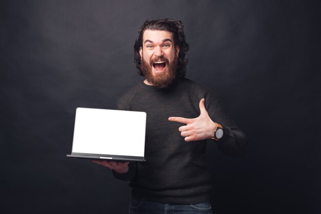 Foto de um homem barbudo espantado gritando e apontando para uma tela em branco no laptop