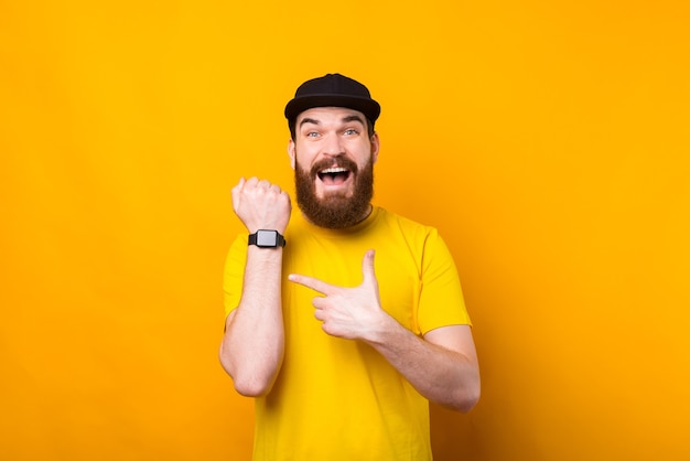 Foto de um homem barbudo hippie surpreso com uma camiseta amarela apontando para seu novo smartwatch