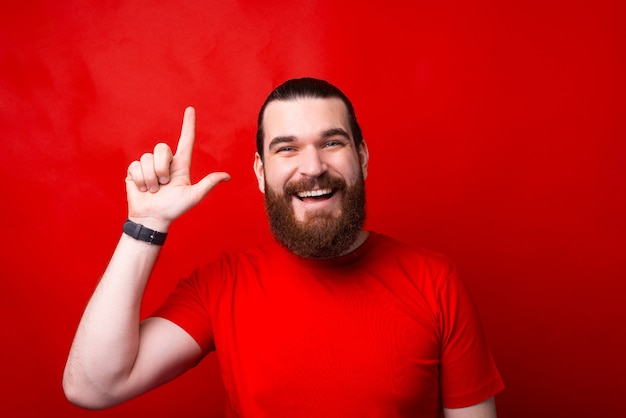 Foto foto de um homem barbudo surpreso apontando para uma parede vermelha