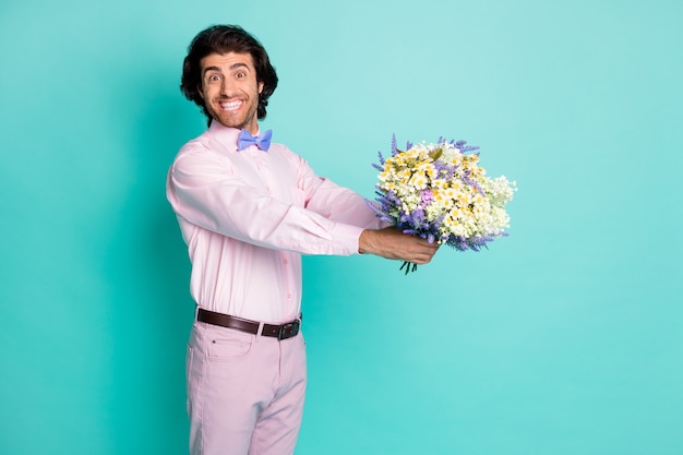 Foto de um homem bonito e sorridente usando uma roupa rosa apresentando buquê de flores, festa de aniversário, cor de azul-petróleo isolada no fundo