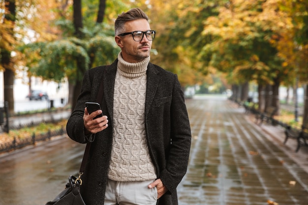 Foto de um homem caucasiano de 30 anos, vestindo roupas quentes, caminhando ao ar livre pelo parque outono