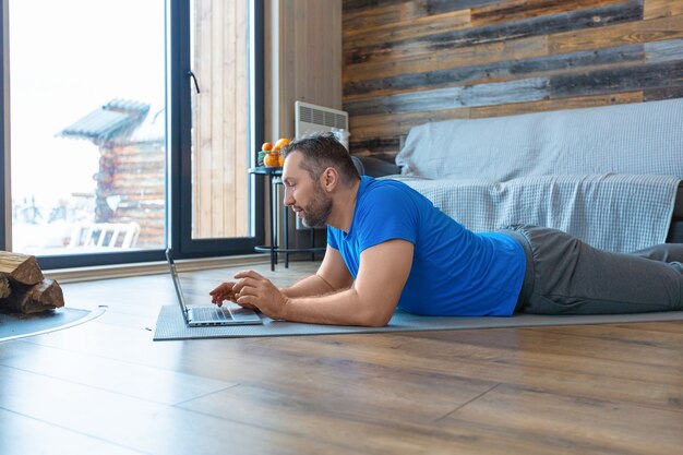 Foto de um homem de meia-idade durante uma videochamada online. Ele está deitado no chão diante de um monitor de laptop.