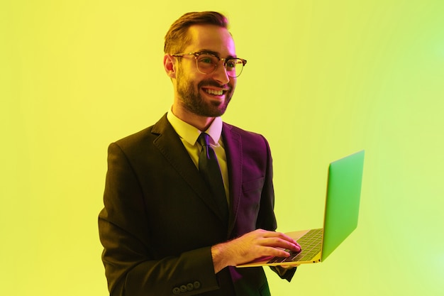 Foto de um homem de negócios jovem feliz otimista satisfeito positivo posando isolado sobre a parede de parede verde clara com luzes de néon led usando o computador portátil.