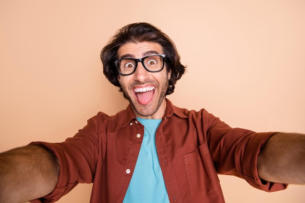 Foto de um homem feliz tirando uma selfie mostrando a língua isolada em um fundo bege pastel