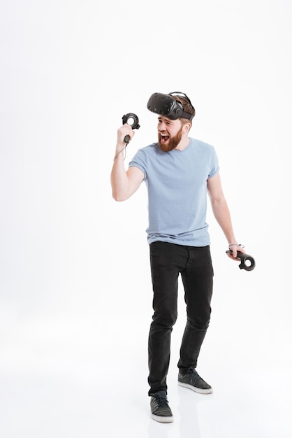 Foto de um homem feliz vencedor usando um dispositivo de realidade virtual em pé com joysticks.