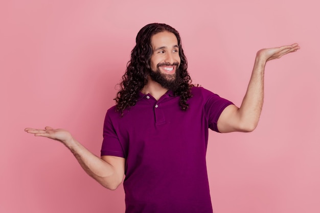 Foto de um homem inteligente segurando um espaço vazio mostrar variante de vantagem usar uma camiseta violeta isolada em um fundo de cor rosa