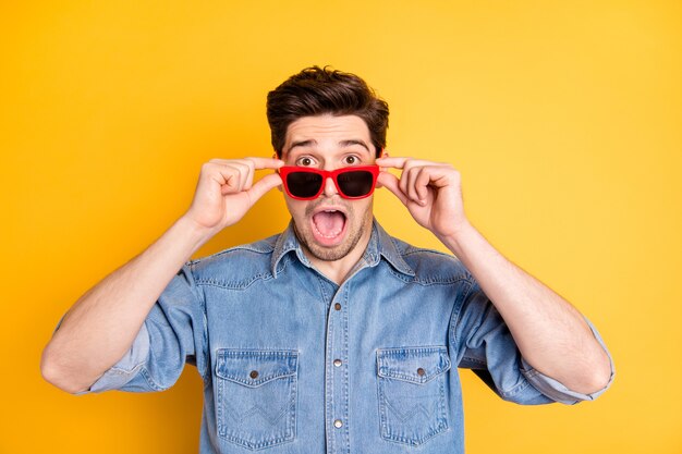 Foto de um homem louco de estupor usando óculos de sol vermelhos chocado com as vendas de óculos com parede de cores vivas isoladas