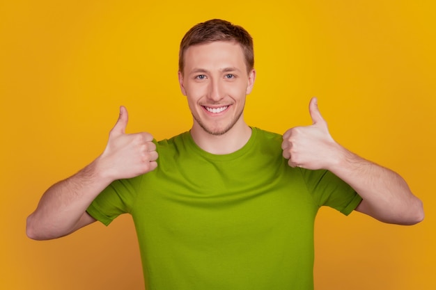 Foto de um jovem animado feliz com um sorriso positivo mostra o polegar legal como um anúncio perfeito isolado sobre um fundo de cor amarela