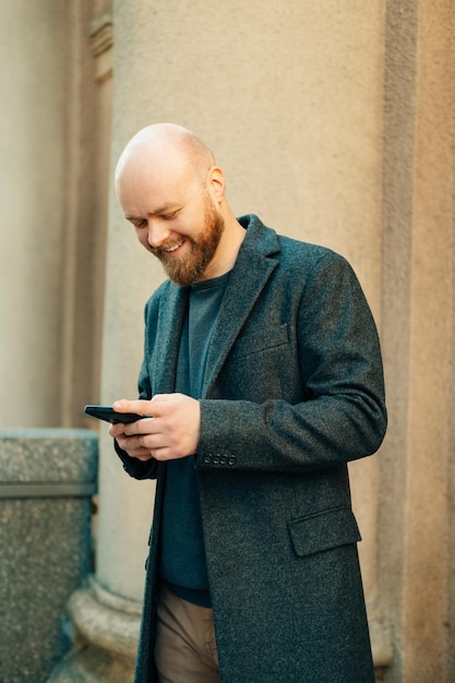 Foto de um jovem barbudo bonito parado ao ar livre na velha cidade europeia e usando smartphone