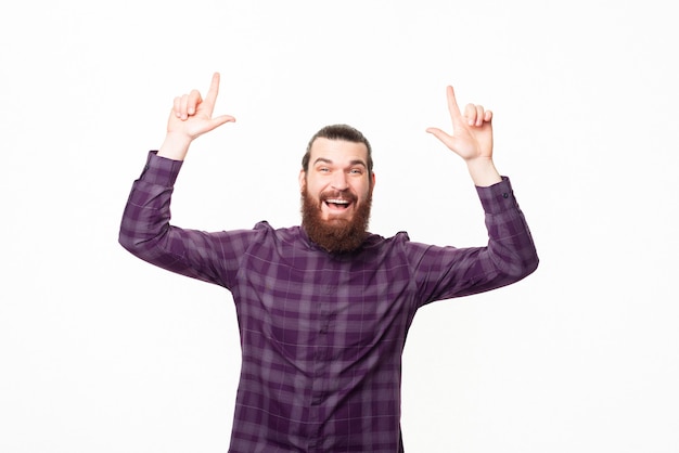 Foto de um jovem barbudo feliz e otimista apontando para cima