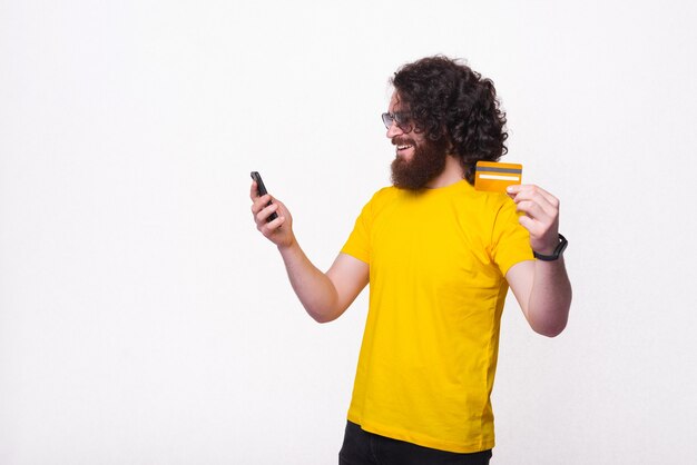 Foto de um jovem barbudo hippie com cabelo comprido e encaracolado usando smartphone e pagando online com cartão de débito