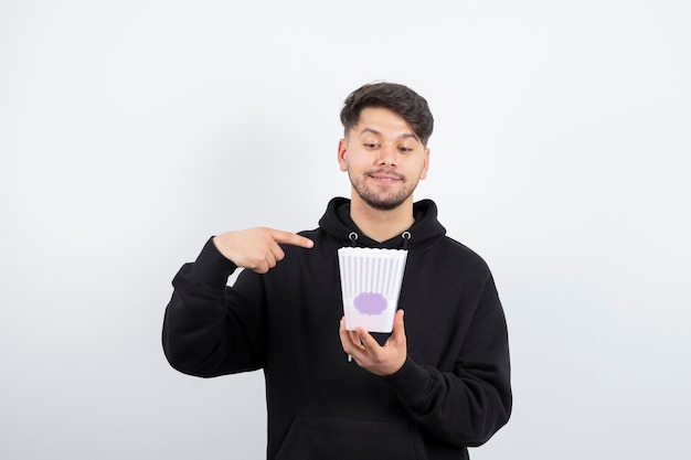 Foto de um jovem bonito assistindo a uma série de televisão e segurando um balde de pipoca