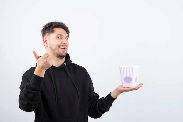 Foto de um jovem bonito assistindo a uma série de televisão e segurando um balde de pipoca