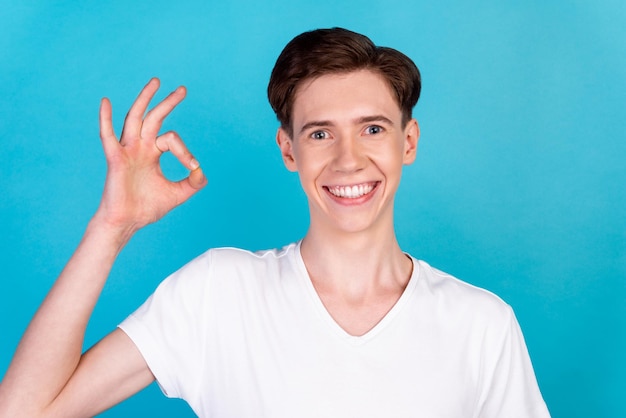 Foto de um jovem bonito mostra os dedos okey símbolo aprova a qualidade bem isolada sobre o fundo de cor azul