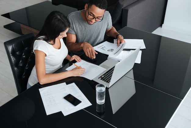 Foto de um jovem casal amoroso feliz usando laptop e analisando suas finanças com documentos. olhe para os papéis.