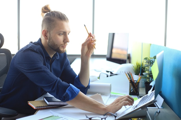 Foto de um jovem designer trabalhando com algumas plantas e um laptop.