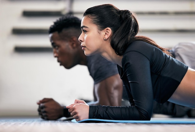 Foto de um jovem e uma mulher fazendo exercícios de prancha em uma academia