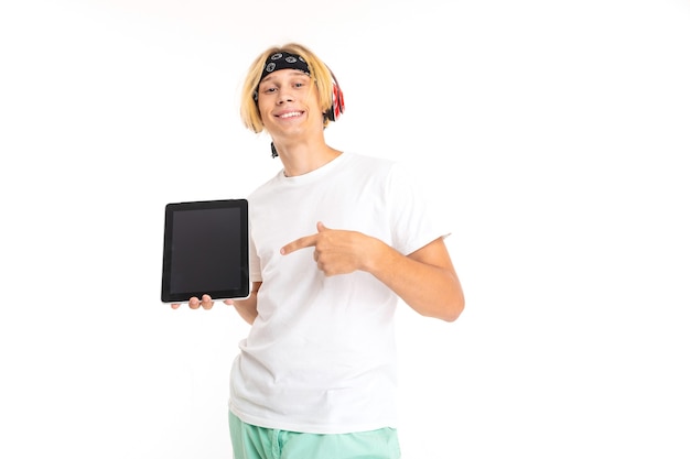 Foto de um jovem homem branco com cabelo loiro, em shorts e camiseta branca segurando um tablet e sorrindo