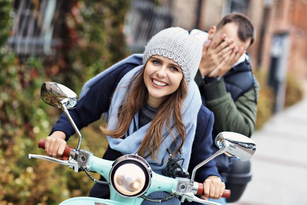 Foto de um lindo casal jovem sorrindo enquanto andava de scooter na cidade no outono