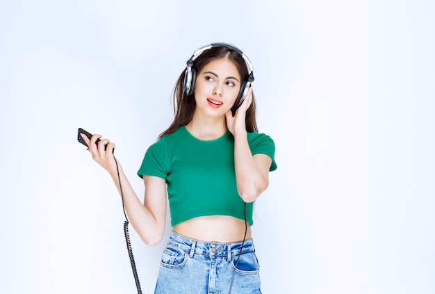 Foto de um modelo de menina bonita com fones de ouvido, segurando o telefone celular.