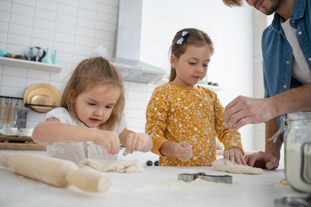 Foto de um pai sorridente e filhas assando na cozinha e se divertindo.