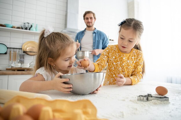 Foto de um pai sorridente e filhas assando na cozinha e se divertindo.