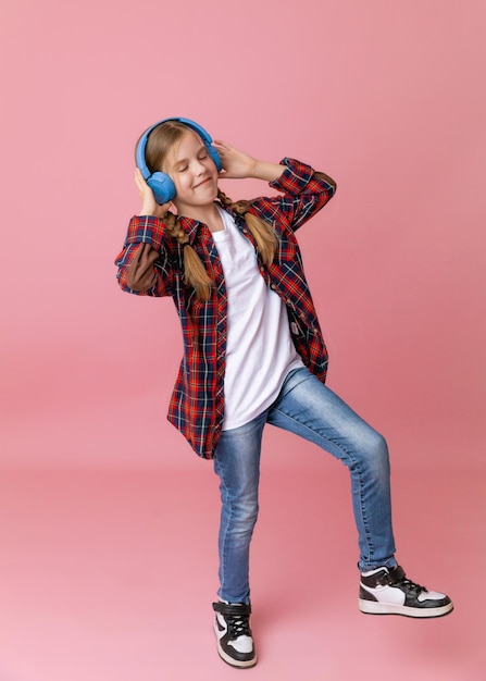 Foto de uma adolescente engraçada e fofa em fones de ouvido de jumper rosa dançando curtindo música em um fundo