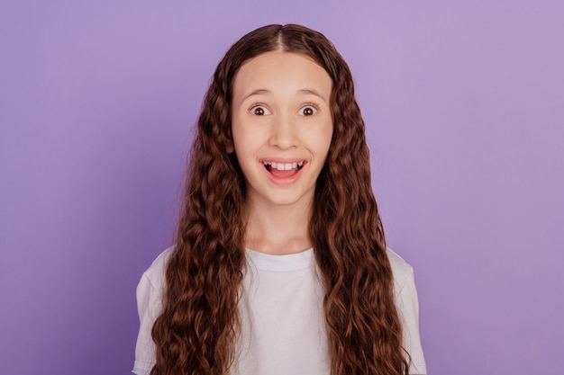 Foto de uma alegre garota pré-adolescente espantada com notícias isoladas sobre fundo roxo